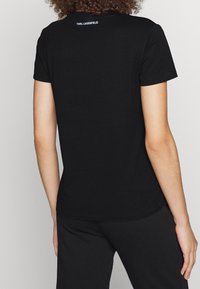 Camiseta negra de cuello redondo, con mangas cortas y detalle de logo en la parte posterior. Fabricada en algodón con una textura suave y corte regular.