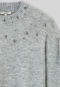 Pull en gris en tricot texturé, présentant des embellissements de petits accents métalliques sur le devant et un col côtelé.