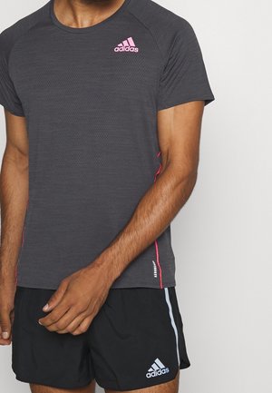 Homme portant un t-shirt Adidas gris foncé avec un logo rose et un short Adidas noir avec un logo blanc et une bande bleu clair.