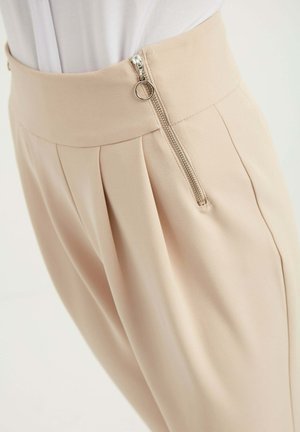 Beige geplooide broeken met een hoge tailleband, zilveren ritsdetails en een gladde stofstructuur. Minimalistisch ontwerp met functionele accenten.