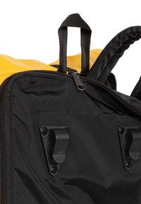 Svart tygryggsäck med gula detaljer. Har två tygöglor upptill, dragkedjor och svart plastfäste på sidorna.