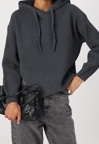 Grijze gebreide hoodie met een textuurpatroon en een buidelzak. Draag het met hoge taille grijze jeans en een zwarte handtas met kettingaccenten.