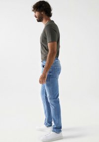 Jeans de mezclilla azul claro con corte ajustado, combinados con una camiseta de manga corta gris oscuro y zapatillas blancas. Textura de tela suave.