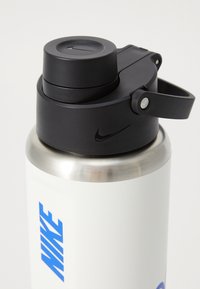 Hvid rustfrit stål vandflaske med en sort trykknaplåg og et håndtag. Udstyret med blå "NIKE" tekst på siden. Glat mat finish.