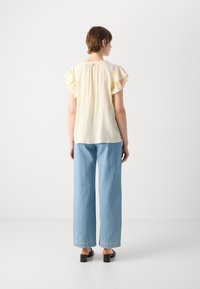 Lys gul, lett topp med rynkete korte ermer, kombinert med høy midje, løstsittende lyseblå jeans og svarte sandaler med blokkhæl.
