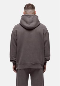 Przeciętny szary hoodie w rozmiarze oversize, wykonany z miękkiego materiału, z kapturem ze sznurkiem, ściągaczami w mankietach i na dole oraz luźnym krojem o gładkiej fakturze.