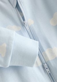 Jasnoniebieski zapinany na zamek ubranie z miękkimi wzorami chmur, ściągaczami na rękawach i gładkim zamkiem błyskawicznym. Delikatnie teksturowana bawełniana tkanina.