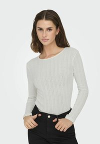 Long-sleeve white ribbed top with a scoop neckline, featuring subtle textured patterns and fitted design, paired with high-waisted black pants.