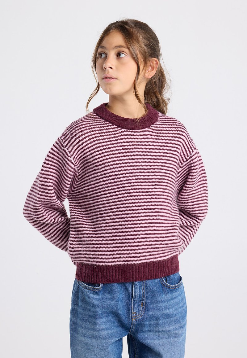 Raidallisen puseron sävyt vaaleanpunainen ja burgundi, jossa on ribbineck ja hihansuut, valmistettu teksturoidusta neuleesta. Yhdistetty sinisiin farkkuihin.