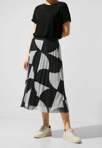 Svart och vit plisserad kjol med abstrakt mönster, matchad med en svart t-shirt med kort ärm och beige sneakers. Slät tyg, medellång.