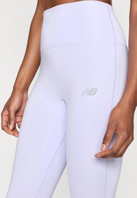 Ανοιχτό μοβ κολάν με ψηλή μέση από ελαστικό ύφασμα, με ραφές flatlock και αντανακλαστικό λογότυπο στο μηρό.