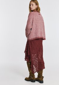 Rožnat puhast pulover, oblečen čez bordo čipkasto krilo z asimetričnim robom, kombiniran z rjavimi škornji do kolen z zaponkami.