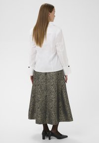 Bijela košulja dugih rukava s crnim gumbima, u kombinaciji s uzorkovanom tamnozelenom i zlatnom suknjom do gležnjeva. Crne štikle upotpunjuju look.