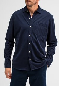 Navyblauwe blouse met lange mouwen, gemaakt van zachte stof, met een knoopsluiting kraag, een borstzak en witte knopen op de knoopsluiting.