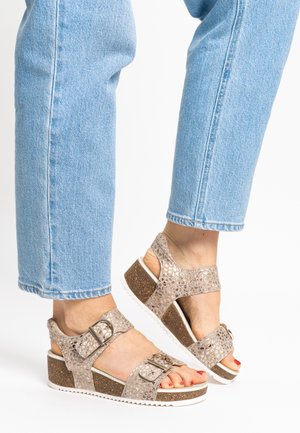 Strappy wedge sandals in metallic beige with textured upper, adjustable buckles, cork-like platform, and white outsole.