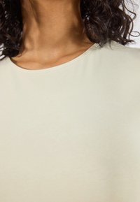Top verde claro de manga corta y cuello redondo. Hecho de una tela suave y lisa con detalles de costura visibles en el collar.
