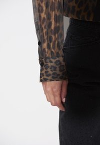 Sheer blouse met luipaardprint en zwarte knopen bij de mouwen, gecombineerd met een zwarte rok van textuurstof met stippenaccenten.