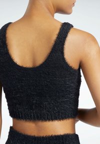 Svart cropped topp laget av myk, fluffy stoff. Har brede stropper og rund halslinje, med en teksturert finish langs kantene.