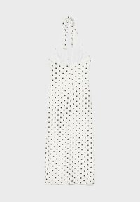 Robe blanche dos nu à pois noirs, corsage ajusté et longue jupe fluide sur un fond clair uni.