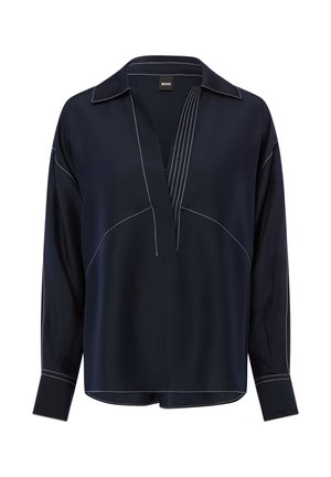 Blouse bleu marine foncé à manches longues avec surpiqûres blanches contrastantes, col ouvert et patte de boutonnage en V, avec une coupe ample et des poignets boutonnés.