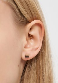 Quadratischer Ohrstecker aus Metall mit einem verlaufenden Finish in Goldtönen, an einem menschlichen Ohr getragen. Subtile Textur und minimalistisches Design.