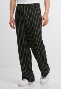 Pantaloni negri cu dungi albe verticale, dintr-un material moale, având un talie elastică și șnur, asortați cu adidași albi.