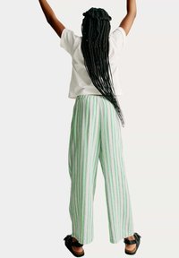 Witte korte mouwen shirt, groen gestreepte wijde broek met roze en blauwe accenten, textuurstof, losse pasvorm, gedragen met zwarte sandalen.