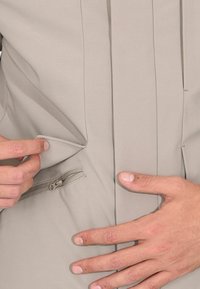 Indumento grigio chiaro con tasca con cerniera e design frontale piegato. Il materiale sembra liscio con sottili dettagli di cucitura.