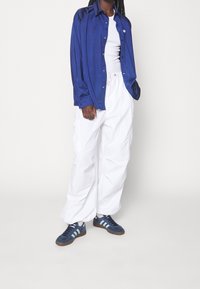 Blue satin long-sleeve shirt, white loose cargo pants, and navy sneakers with blue stripes. Features soft texture and sporty design elements.