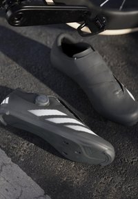 Black cycling shoes with a smooth texture, featuring white diagonal stripes, a BOA dial closure, and textured soles for grip.