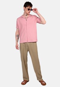Camisa de manga corta de color rosa claro con un patrón texturizado, abotonada en la parte delantera, combinada con pantalones beiges y sandalias marrones.