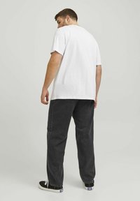 Camiseta blanca de algodón con un corte relajado, combinada con pantalones de mezclilla negros. El conjunto incluye zapatillas casuales con cordones blancos.