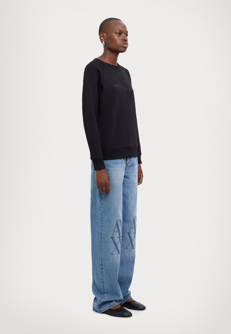 Felpa nera con testo in rilievo, abbinata a jeans a gamba larga blu chiaro con una grafica sottile in blu. Completata con ballerine nere.