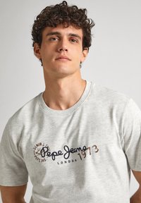 Camiseta de algodón gris con cuello redondo, mangas cortas y un logo frontal que dice "Pepe Jeans London 1973" en colores contrastantes.