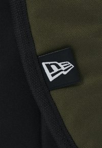 Black and olive green fabric with a textured finish, featuring a white logo tag with a stylized letter and design detail.