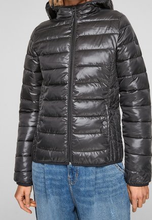 Czarna błyszcząca pikowana kurtka puchowa z kapturem, zapinana z przodu na zamek błyskawiczny, z kieszeniami na zatrzaski, noszona z niebieskimi dżinsami.