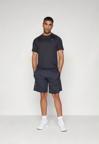 Maglietta a maniche corte di colore grigio scuro che assorbe l'umidità e pantaloncini abbinati. Il tessuto sembra leggero. Scarpe da ginnastica bianche e calzini bianchi.