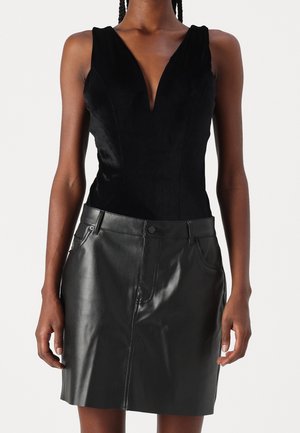 Woman wearing a sleeveless black velvet top with deep V-neck and a black leather skirt with front seam and pockets.
