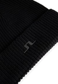 Svart stickad mössa med ribbad textur och en diskret svart logotypdetalj. Klumpen är tjock och ger värme och täckning.
