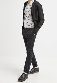 Black cardigan over a white shirt with black animal patterns, paired with dark trousers and black lace-up shoes. Smooth textures and fitted design.