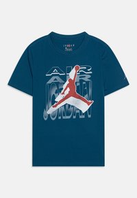 Tyrkysové bavlněné tričko s velkým červeným a bílým grafickým motivem skákající postavy a textem "AIR JORDAN" v vrstveném stylu. Kulatý výstřih.
