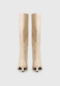 Beige knee-high boots made of glossy material, featuring a fitted design, pointed toe, and a small black heel. Smooth texture with no visible patterns.