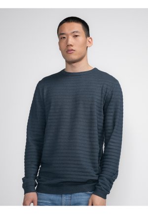 Dark blue textured sweater with horizontal ribbed pattern, round neck, long sleeves, and fitted cuffs. Worn over jeans.