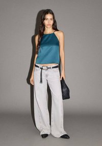 Tamnoplavi satenasti crop top s tankim naramenicama, kombiniran s hlačama širokih nogavica svijetlosive boje visokog struka, crnim remenom s resicama i teksturiranom crnom torbicom.