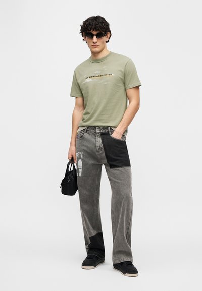 Πράσινο κοντομάνικο μπλουζάκι με γραφικό σχέδιο, συνδυασμένο με μαύρο και γκρι τζιν παντελόνι με ανασηκώσεις. Μαύρα αθλητικά παπούτσια και μικρή τσάντα ολοκληρώνουν την εμφάνιση.