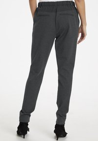 Grå elastiska midjebyxor med slim fit, som har två bakfickor och en mjuk textur, tillsammans med svarta klackskor.