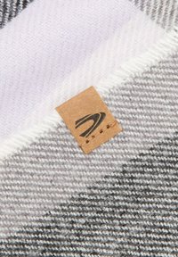 Grå og hvid stribet tekstil med en blød, vævet struktur; har et brun lædermærke med et logo fastgjort.
