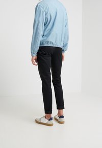 Ljusblå denimjacka, svarta byxor och vita sneakers med grå accenter. Jackan har elastiska manschetter; byxorna är åtsittande med uppvikta fållar.