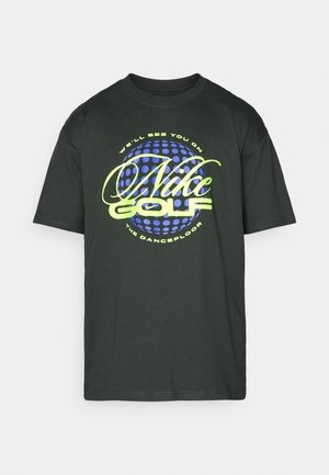 Fekete, rövid ujjú pamut póló. Színes grafikával ellátott "Nike Golf" felirat látható rajta, zöld és kék színekben, kör alakú mintázat háttérrel.