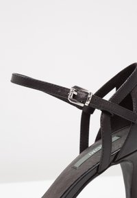 Sandal noir à talons hauts avec une bride et une boucle en argent, texture en cuir lisse et design ouvert.